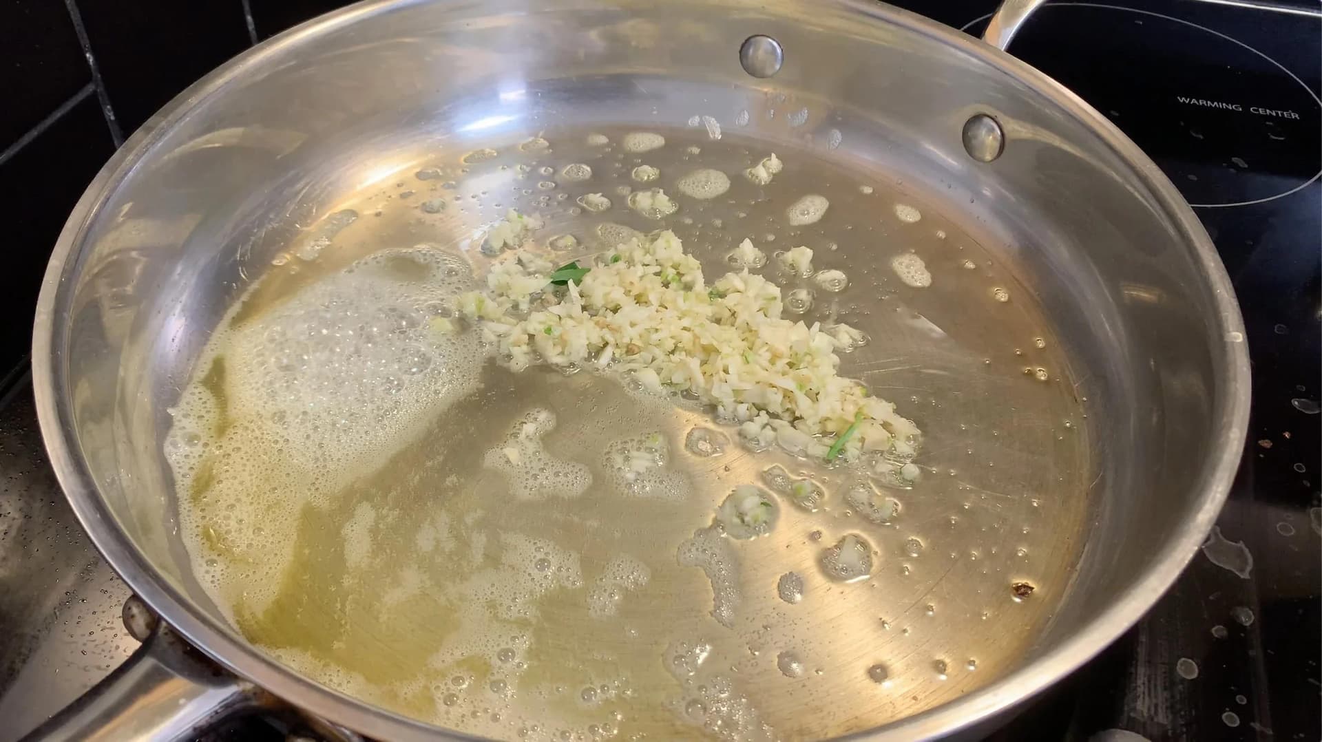Shrimp and minced garlic sautéing in butter and olive oil in a stainless steel pan on stovetop.