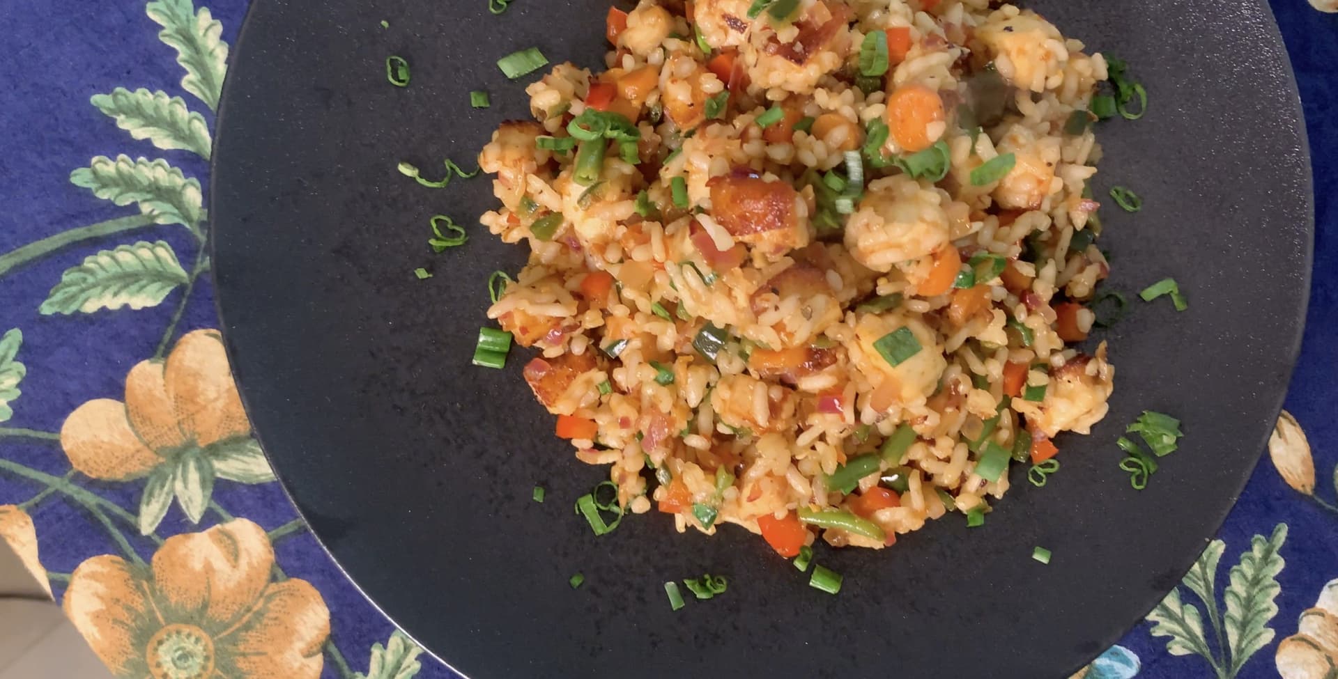 Spicy paneer fried rice garnished with green onions served in a dark bowl on a decorative blue plate.