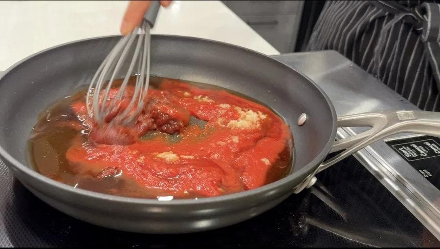 Red Korean sauce being whisked in a gray pan on the stovetop until thickened.