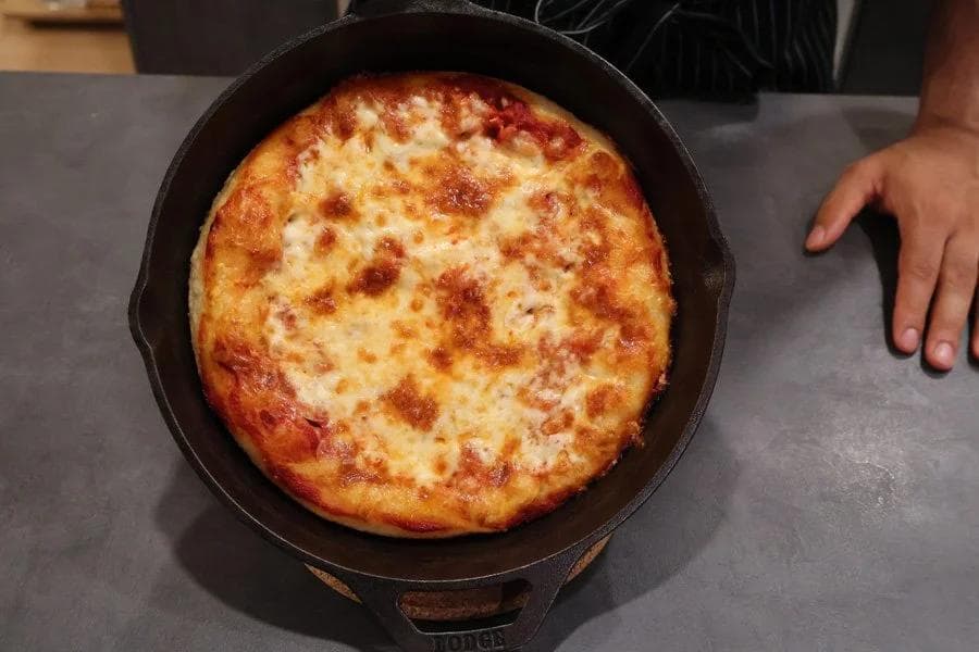 Golden-brown cast iron pan pizza with melted cheese and crispy crust, fresh from cooking.