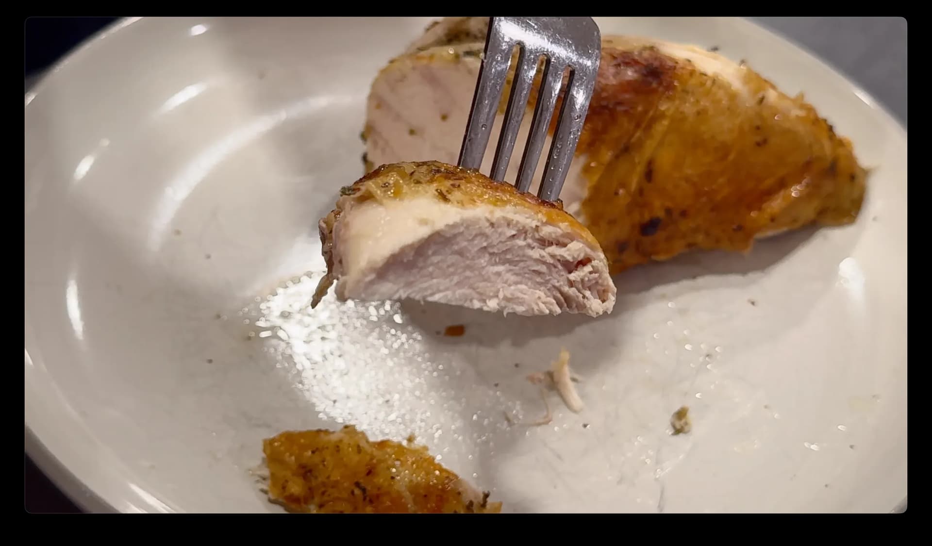 Sliced air fryer chicken breast on a white plate with golden roasted skin, showing juicy pink meat inside, with a fork holding a piece.