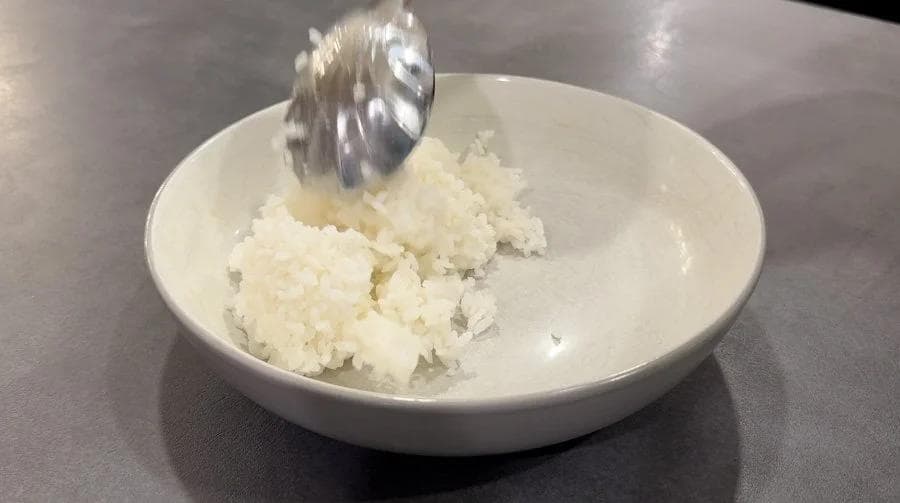 Sushi rice being scooped with a rice paddle into a white bowl for serving with air fryer tofu.