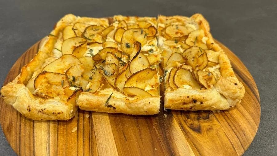 Three slices of golden puff pastry tart topped with thinly sliced potatoes and herbs on a wooden board.