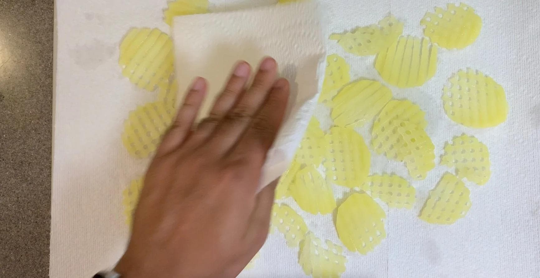 Drained waffle-cut potatoes on paper towel being patted dry by hand.