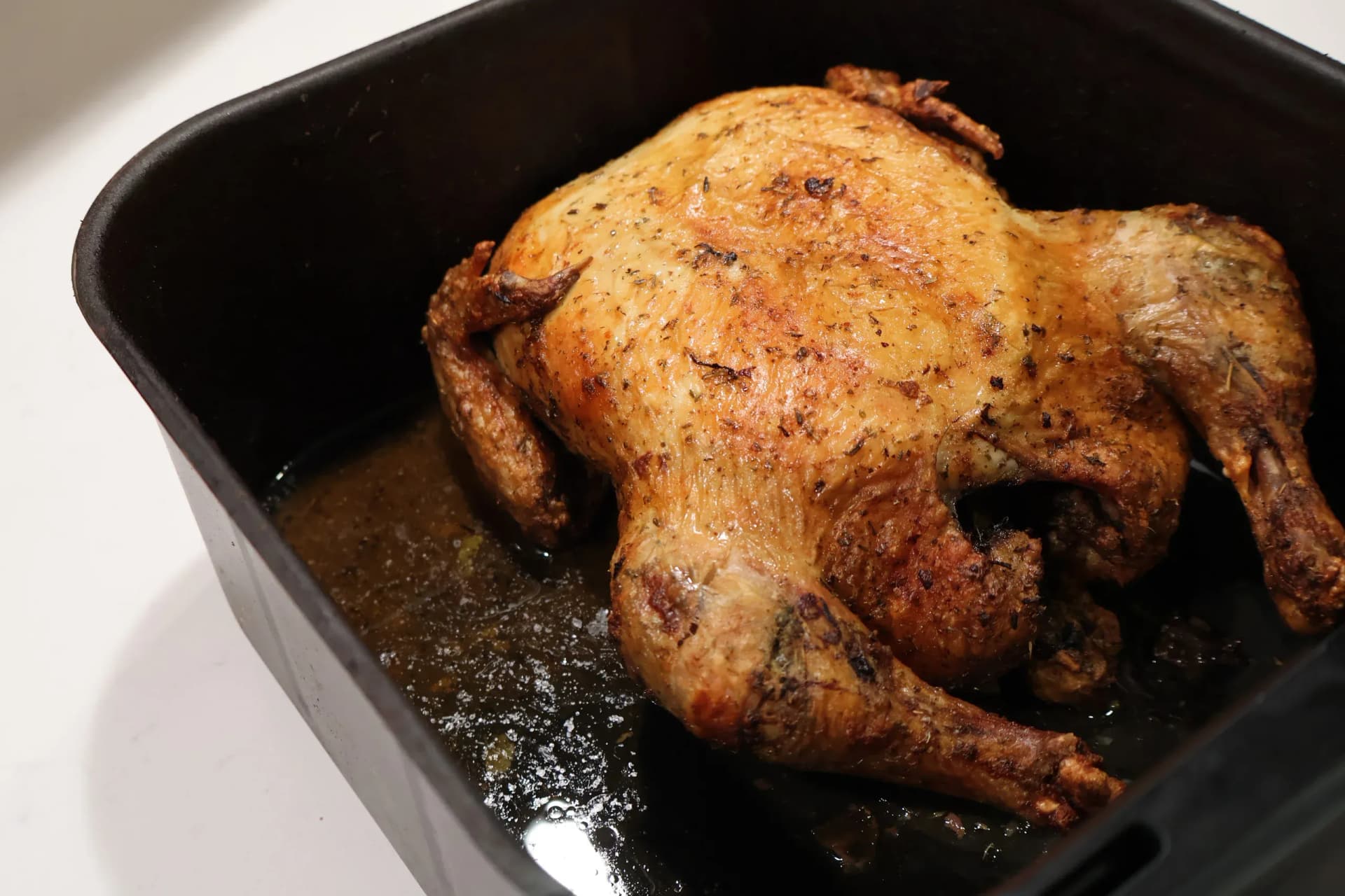 Golden whole chicken sitting breast-side up in the black air fryer basket, juices pooled in the base.
