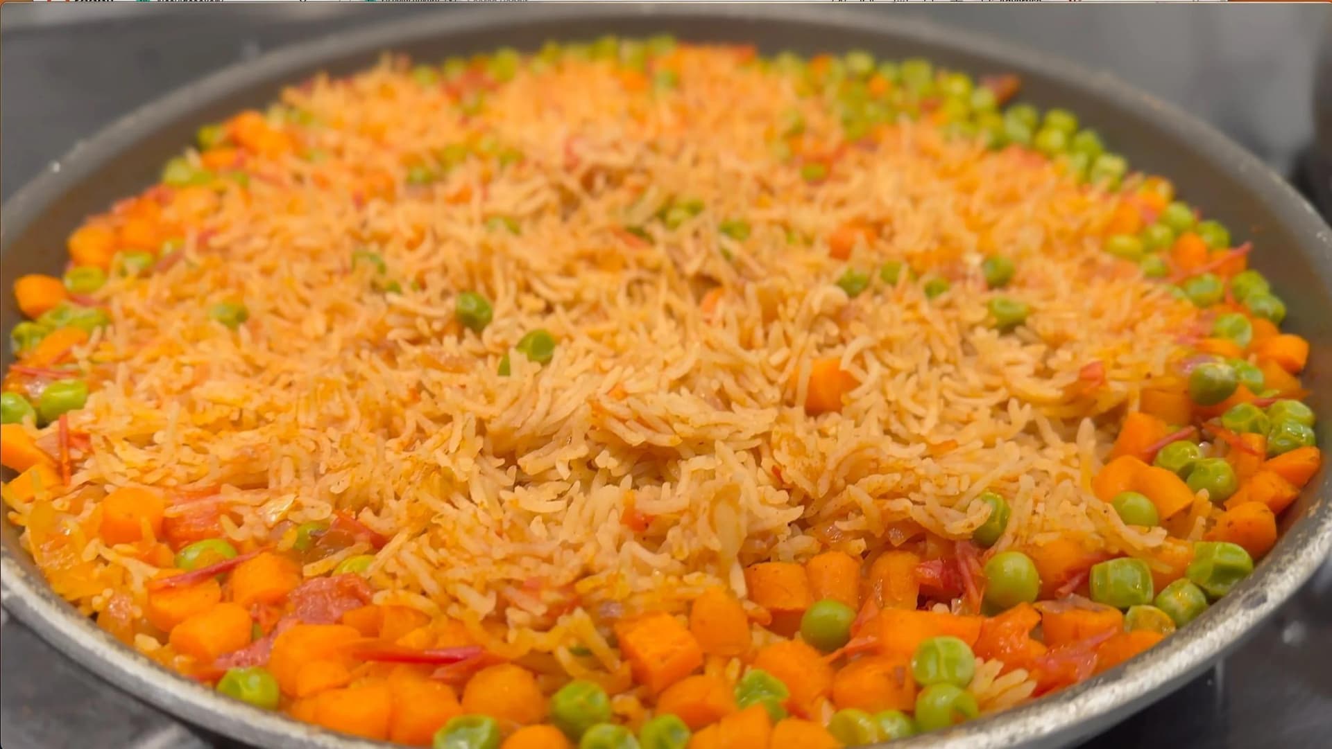 Mexican rice with diced carrots and peas cooking in a skillet with oil.
