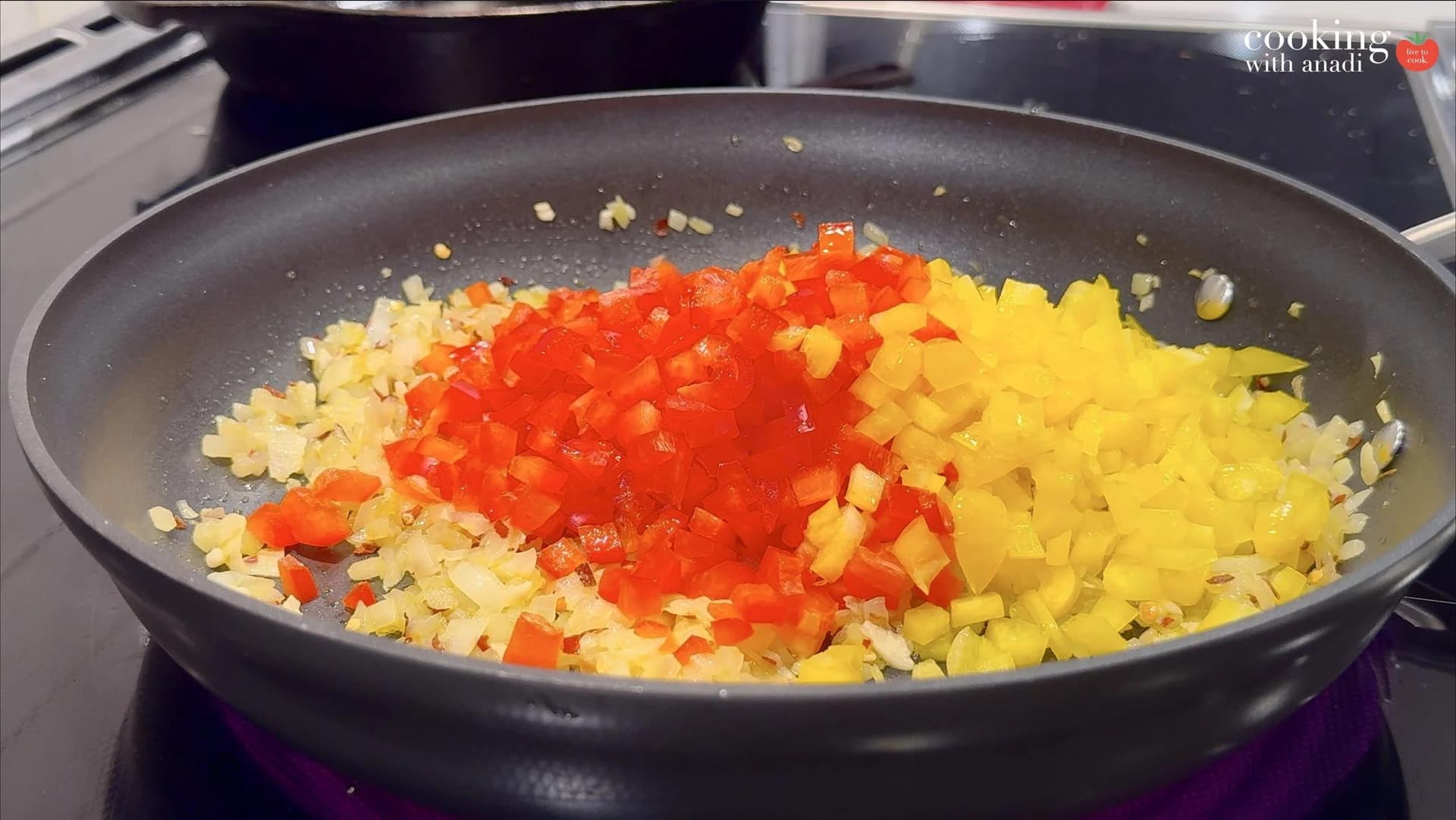 Diced red and yellow bell peppers added to sautéed onions in a dark nonstick skillet.