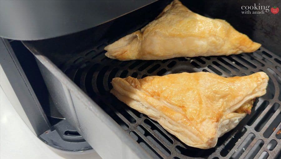 Two golden brown aloo patties in an air fryer basket, puffy and cooked until golden.