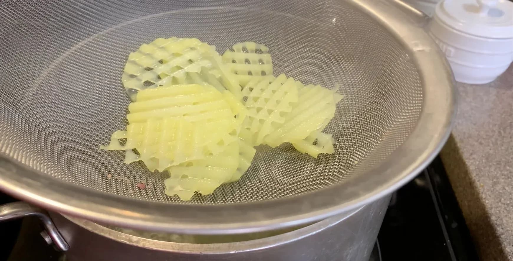 Partially cooked waffle-cut potato slices drained in a colander and patted dry.