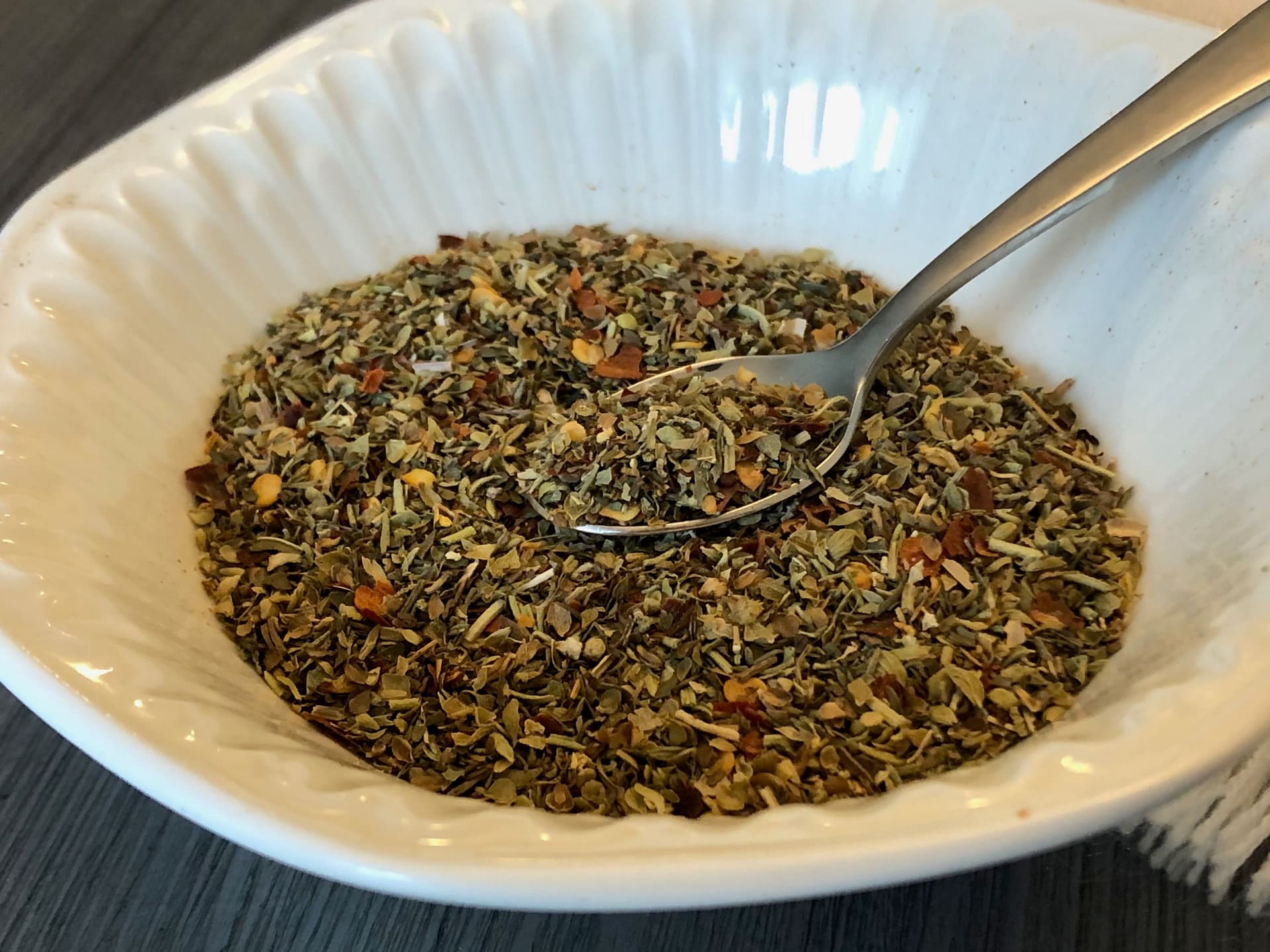 Homemade Italian seasoning blend in white bowl with dried herbs, spices, and orange zest mixed together.