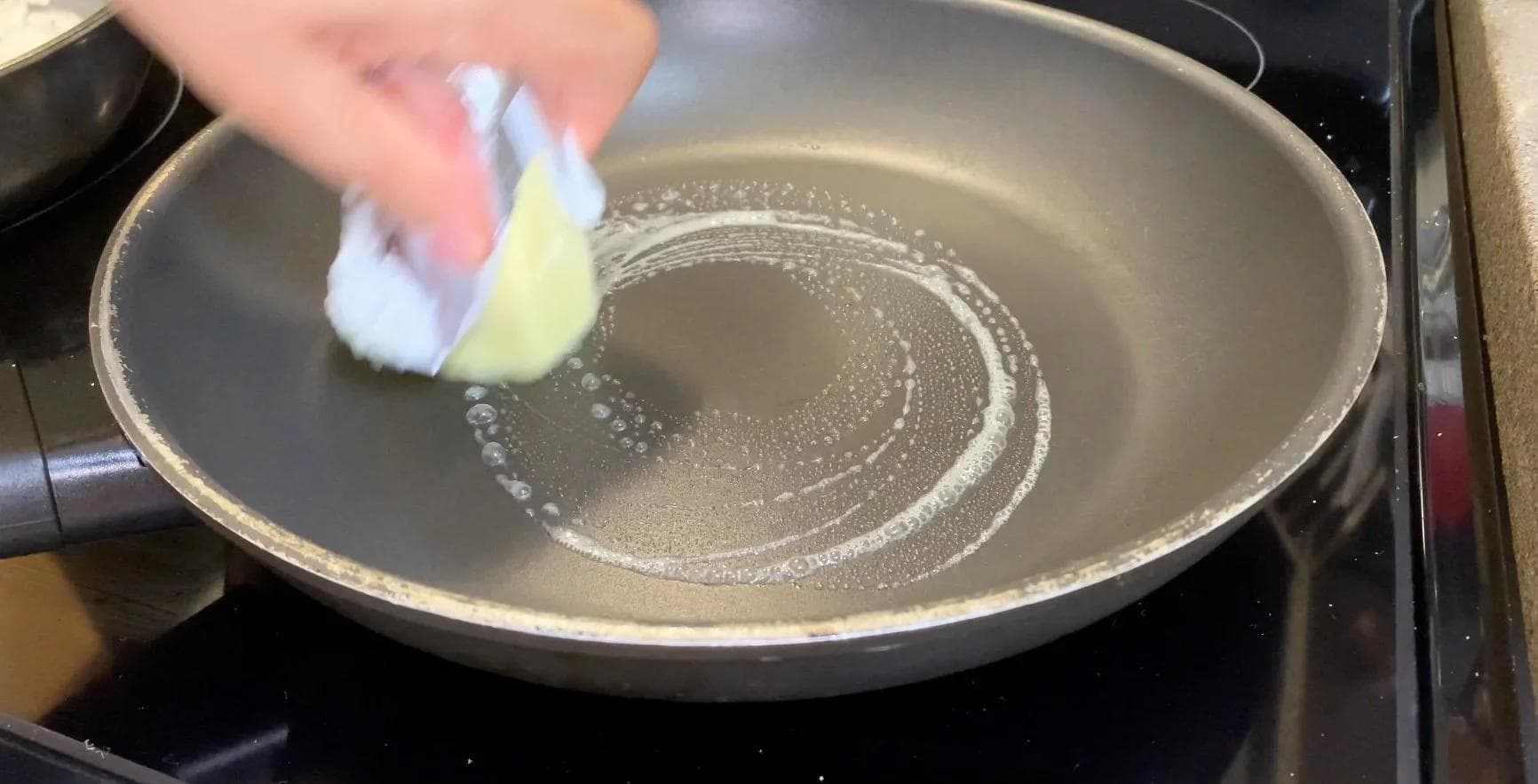 Butter melting in a skillet as a hand holds a slice of bread over the pan to begin toasting a croque monsieur sandwich.