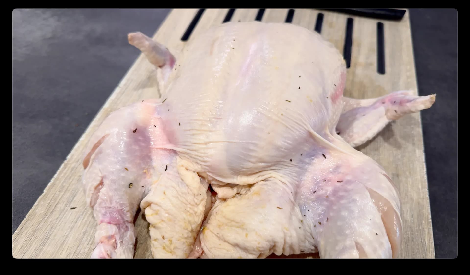 Raw whole chicken on wooden cutting board with slits cut into legs, ready for seasoning