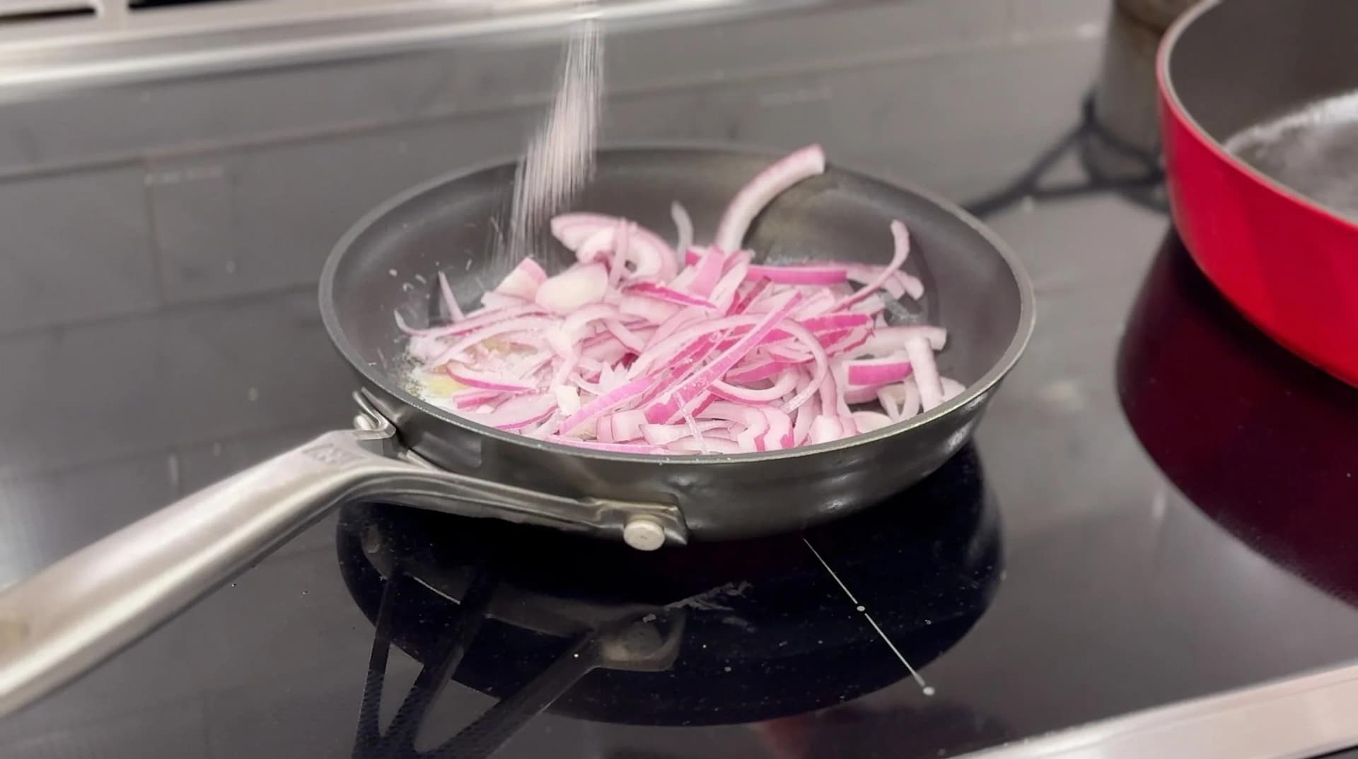 Water being poured over sliced pink onions in a black skillet with melted butter on a stovetop.