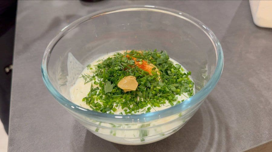Homemade ranch dip ingredients combined in a glass bowl with fresh chopped herbs and garlic on top.