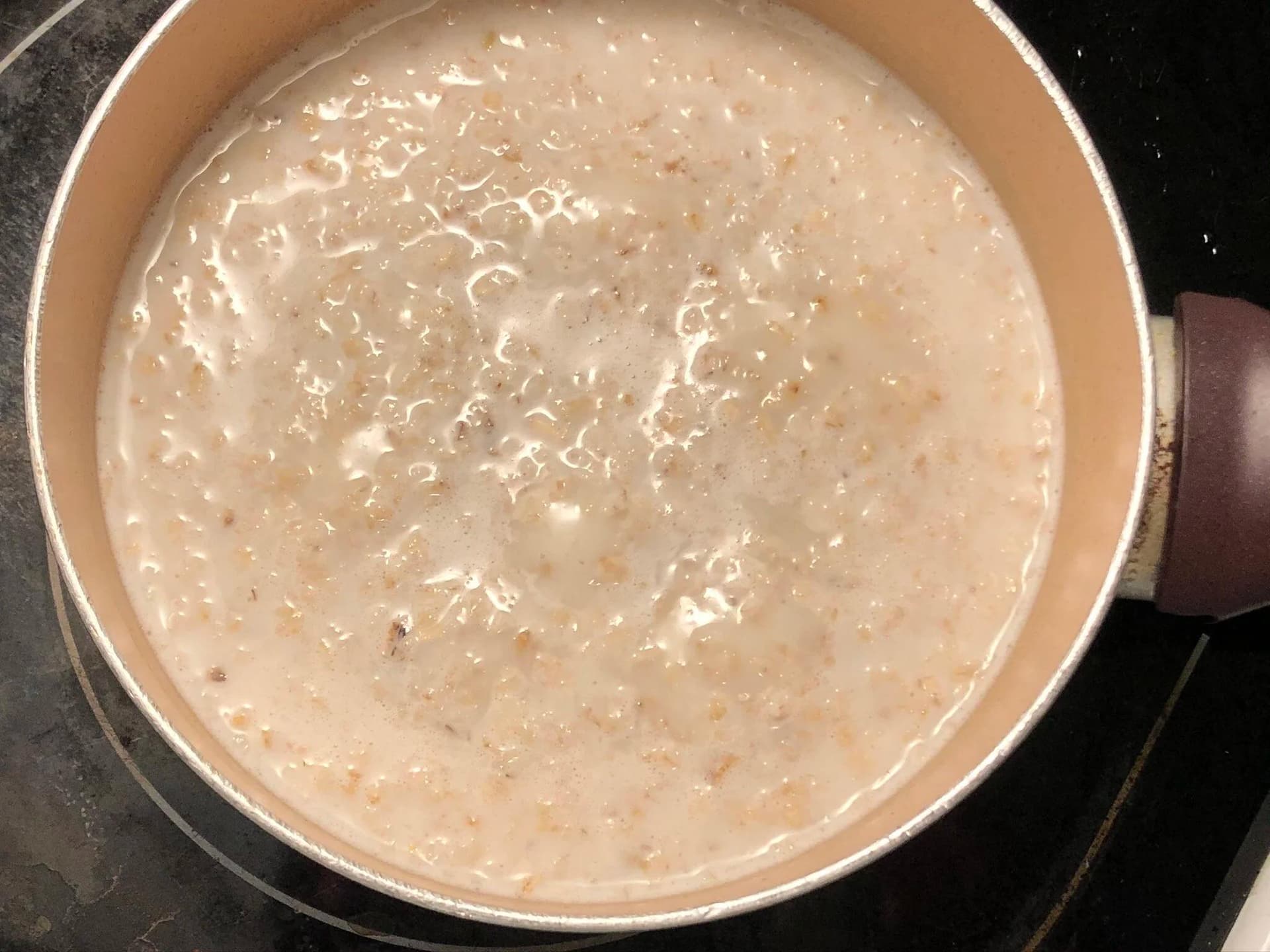 Oatmeal simmering in a pot with milk, showing a creamy beige mixture with bubbles forming on the surface.