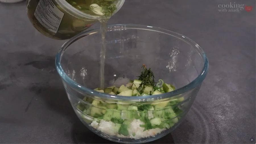 Dressing being poured into a glass bowl containing diced crab, celery, and herbs for crab salad.