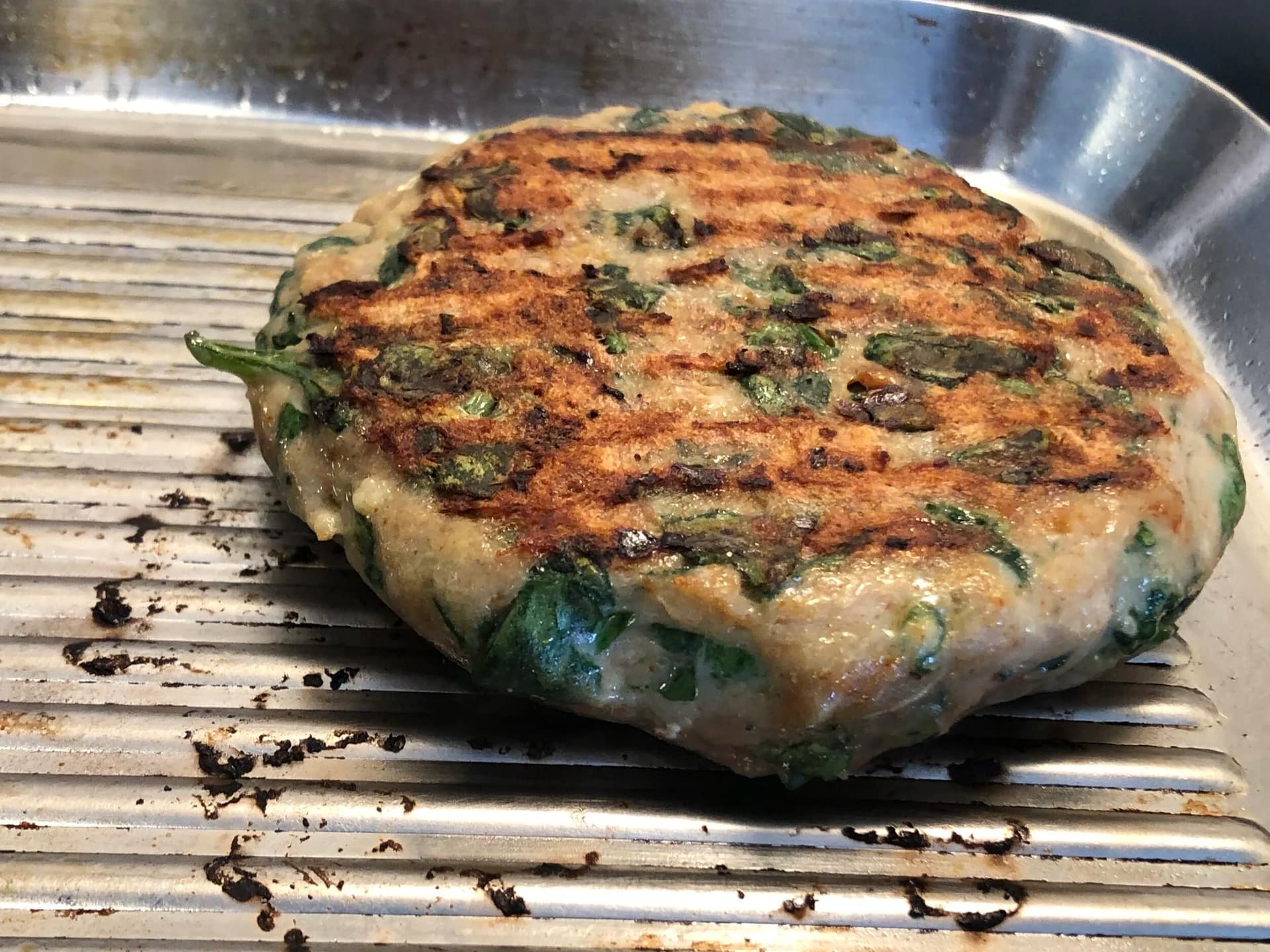 Spinach turkey burger patty cooking on a grill pan, golden brown with melted cheese on top.