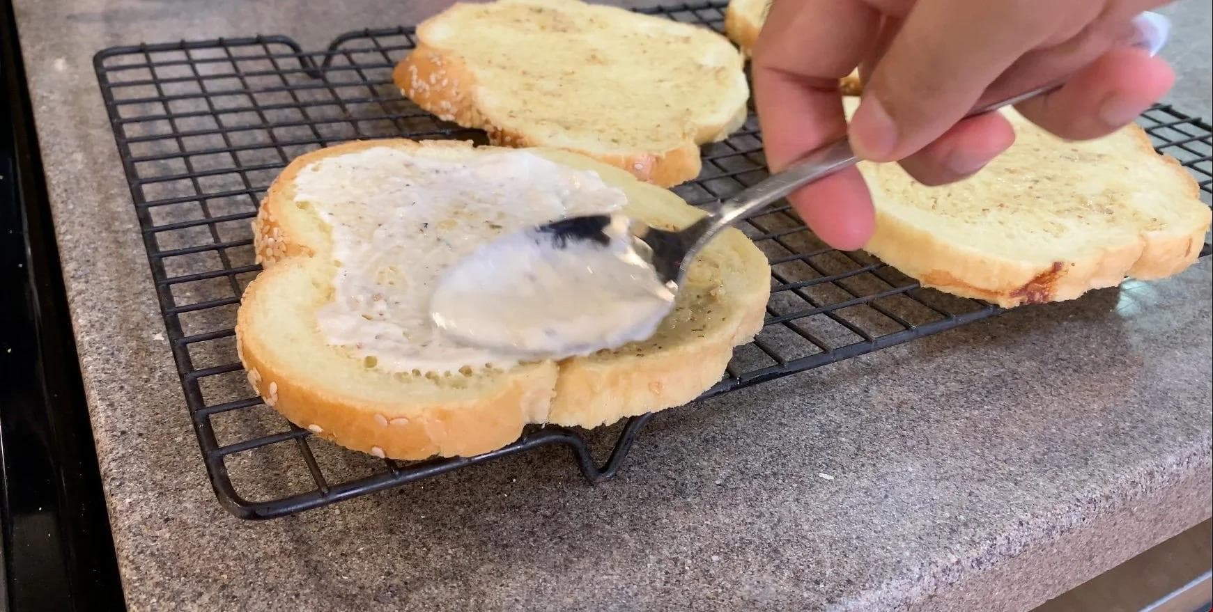 Spreading béchamel sauce on sliced bread with a knife to assemble a Croque Monsieur sandwich.