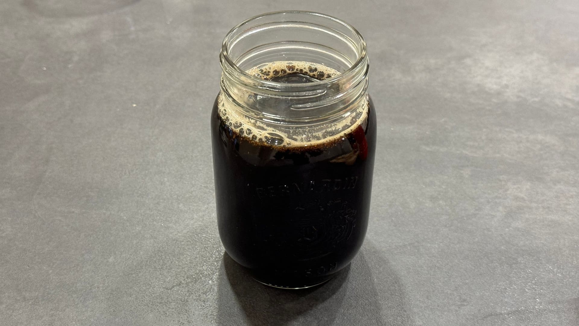Dark gingerbread syrup in a glass jar with foam on top, ready to use.