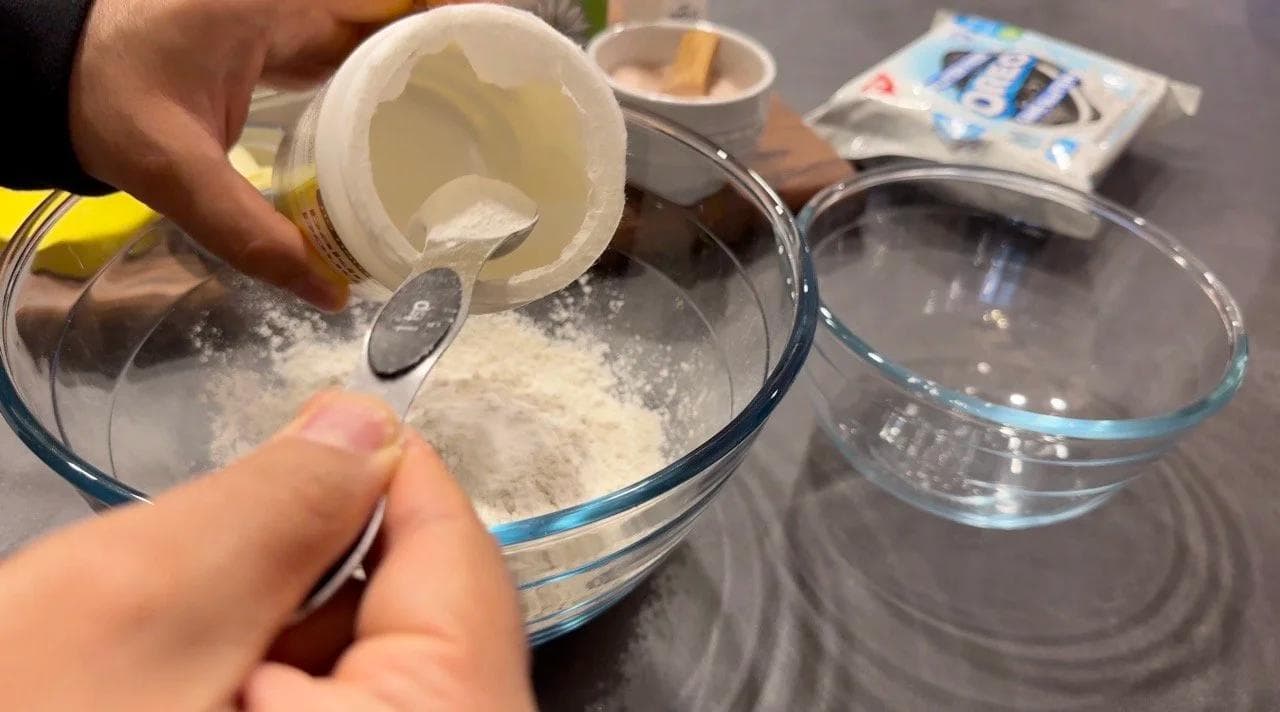 Pouring flour and baking powder into a glass mixing bowl for gluten-free pancake batter.