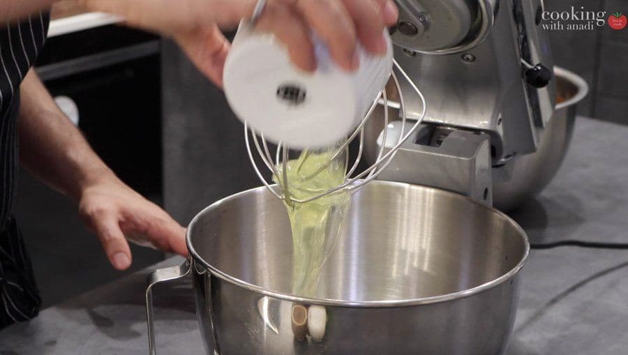 Whipped egg whites being folded into chocolate mixture in a stainless steel bowl with an electric mixer.