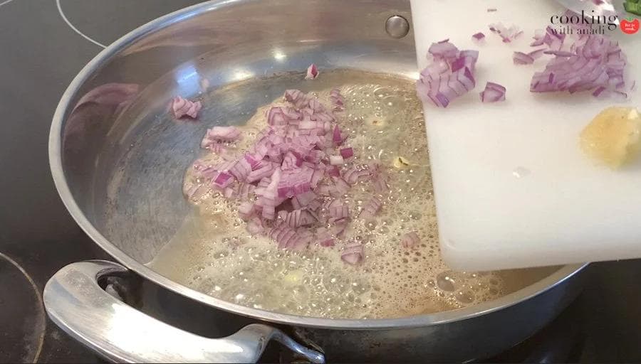 Diced red onions sautéing in melted butter with cumin seeds in a large pan.