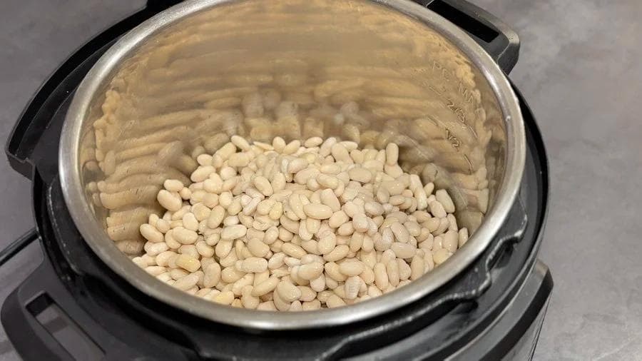 Soaked white beans in an Instant Pot with water, ready for pressure cooking.