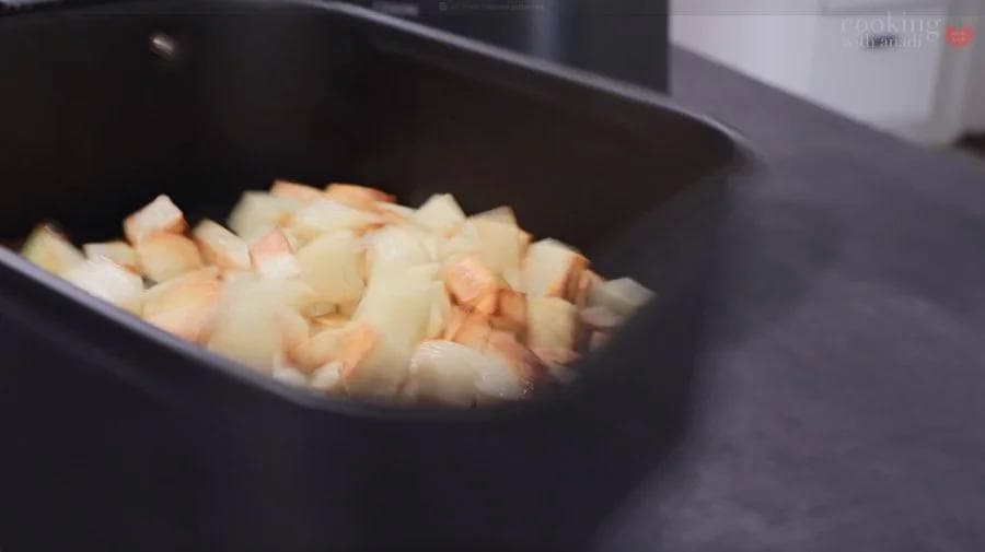 Diced potatoes in an air fryer basket, partially cooked and beginning to brown.