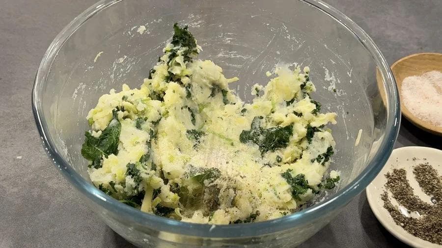Mashed potatoes mixed with chopped greens and cheese in a glass bowl during preparation.