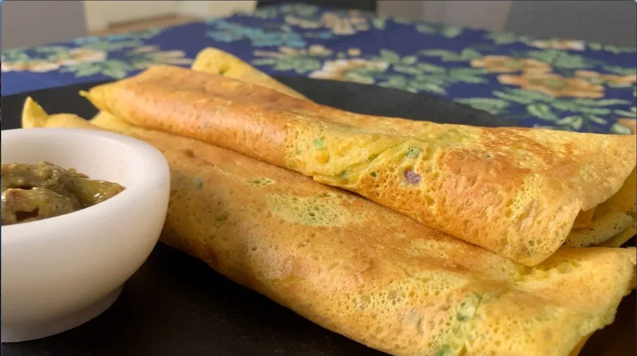 Golden-brown besan chilla pancakes stacked on a plate with a white bowl of green chutney on the side.
