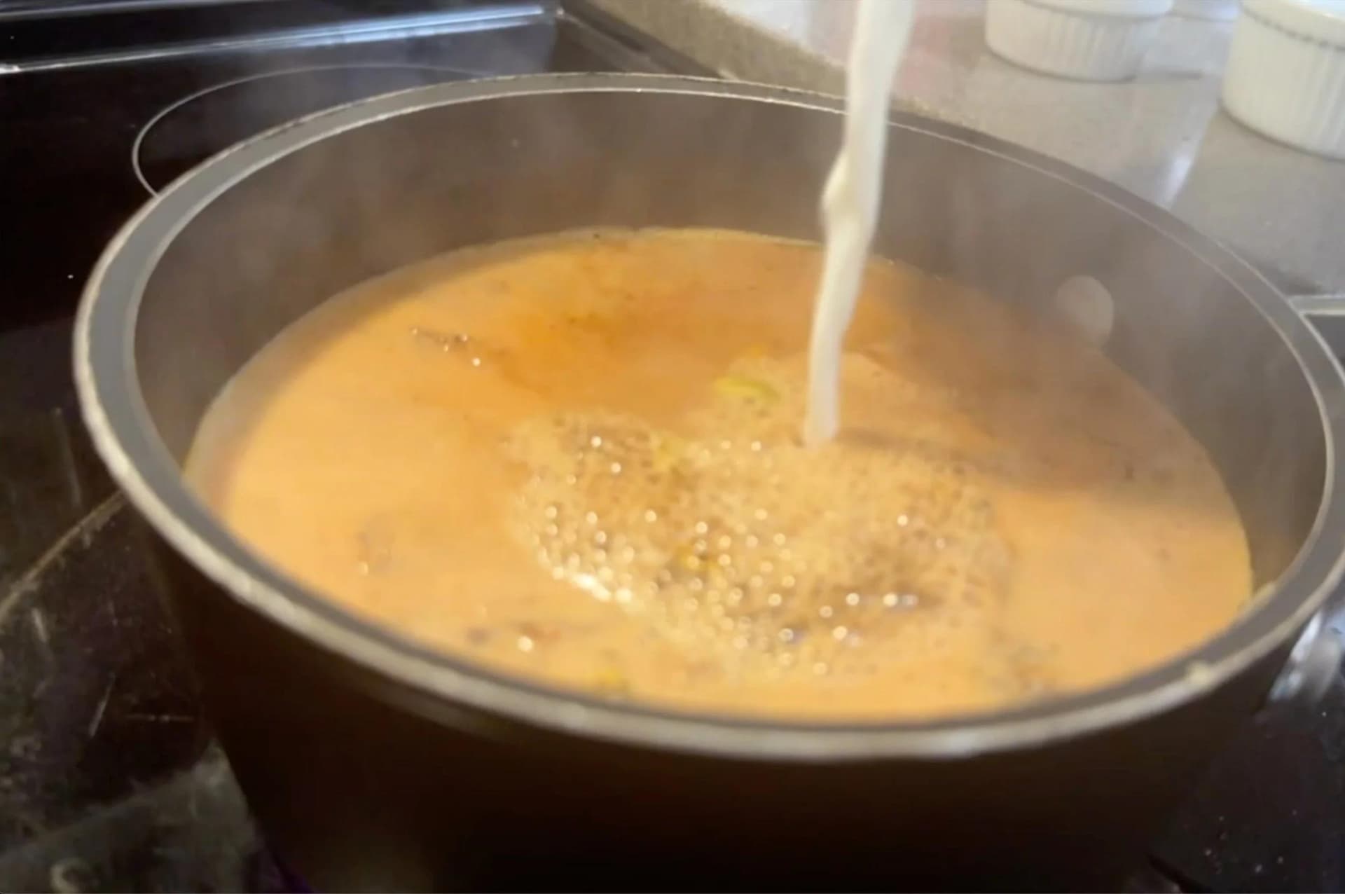 Milk being poured into a saucepan of brewed ginger tea with cardamom and sugar, creating a creamy chai mixture.