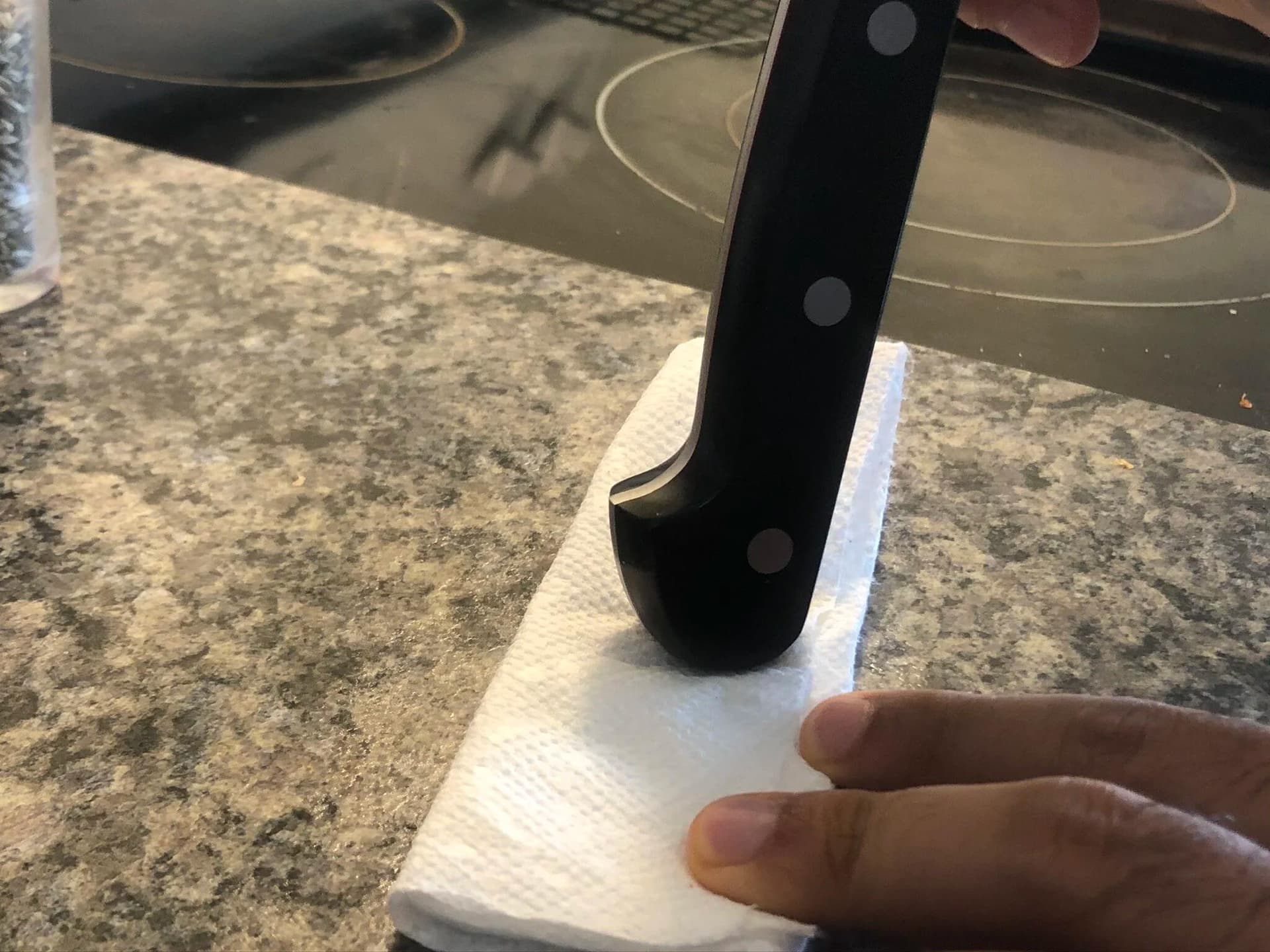Crushing chili seeds with a knife blade on a folded paper towel over a granite countertop.