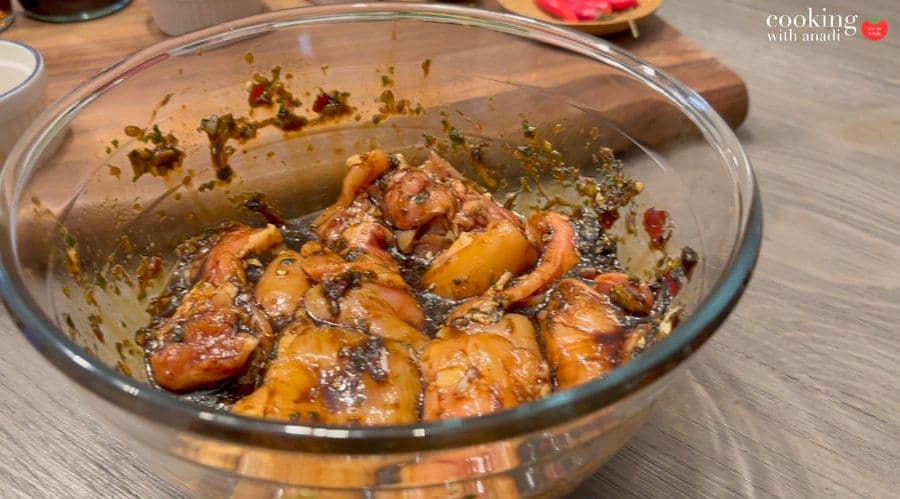 Marinated chicken pieces coated in Thai spice paste in a glass bowl, ready to cook.