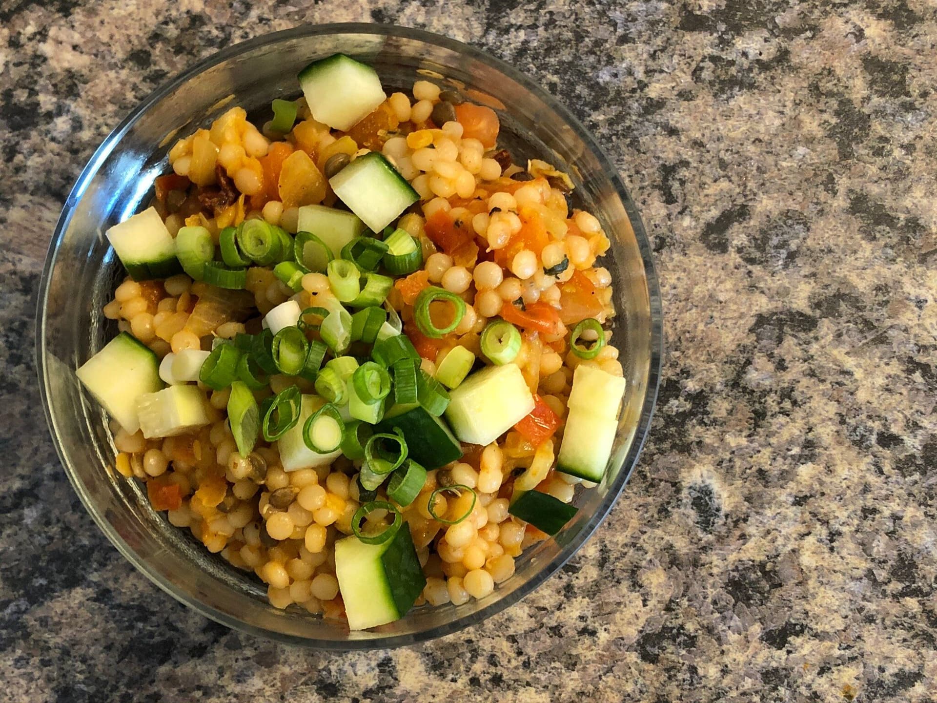 Light vegan couscous salad in a glass bowl with cucumbers, chickpeas, and green onion garnish.