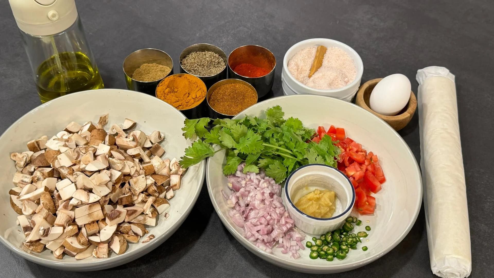 Ingredients for mushroom puff pastry arranged in bowls: diced mushrooms, chopped cilantro, red peppers, minced garlic, diced onions, spices, egg, and olive oil.