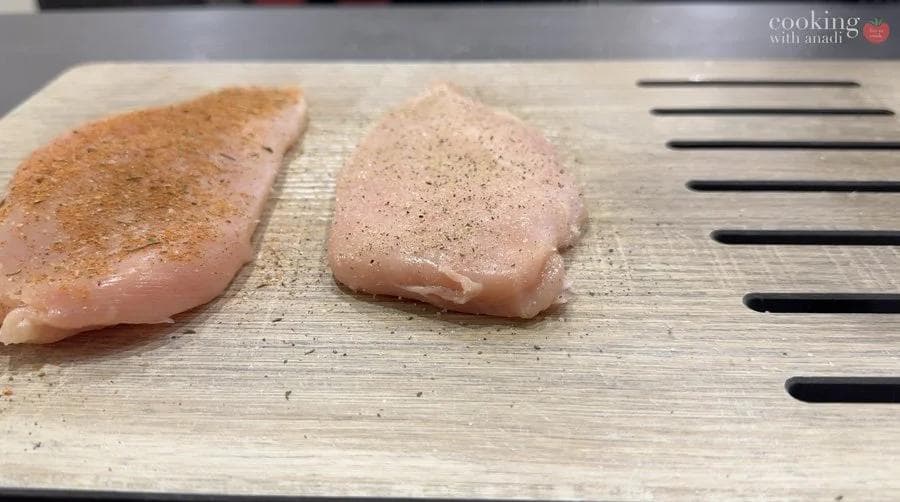 Two seasoned chicken breasts on a wooden cutting board, one with salt and pepper, one with blackening seasoning.