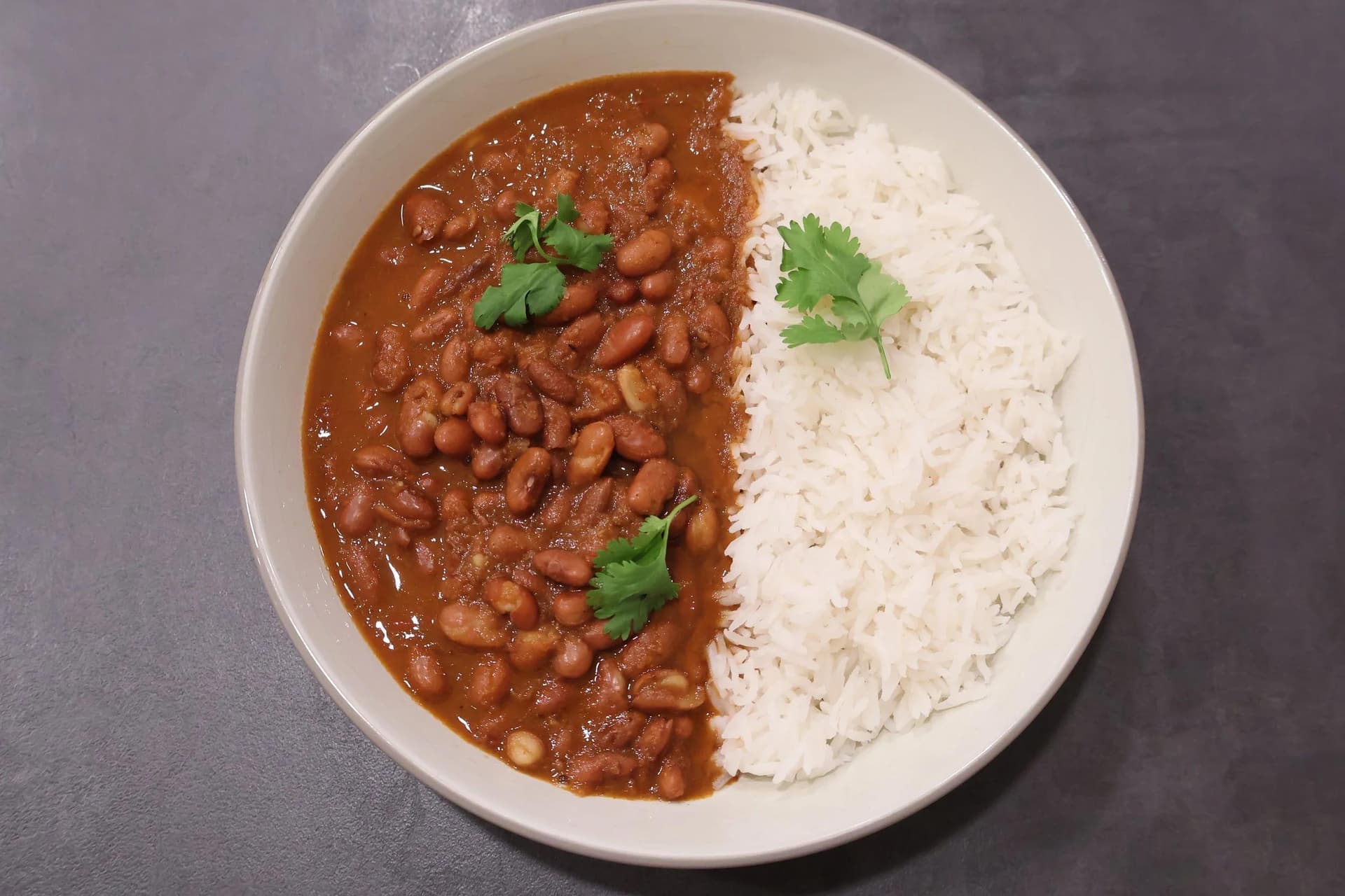 Rajma masala served in a white bowl with white rice, garnished with fresh cilantro leaves.