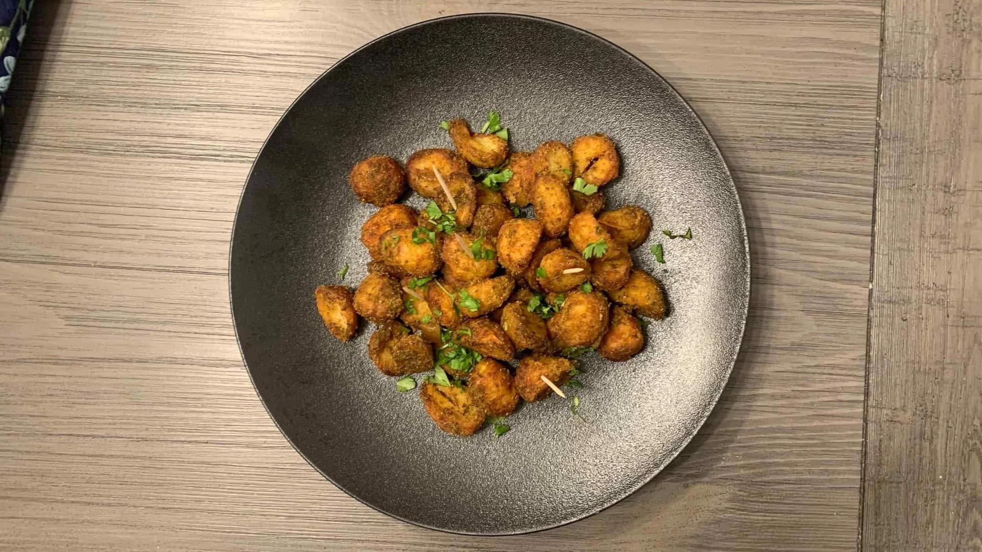 Crispy golden air fryer baby potatoes garnished with fresh green herbs on a dark plate.