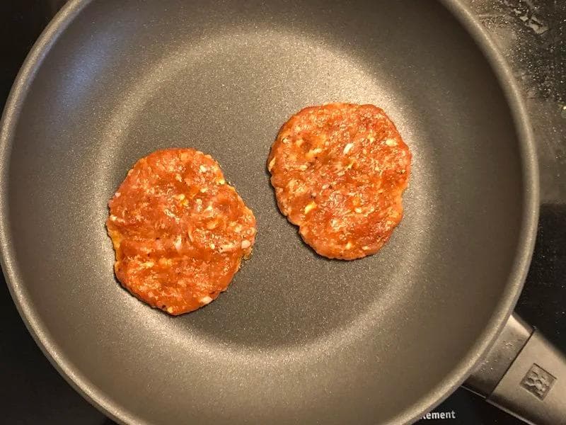 Two cooked turkey sausage patties browning in a nonstick skillet with oil.