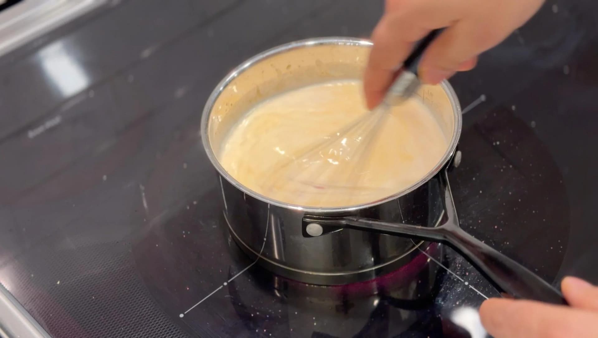 Whisking creamy béchamel sauce in a saucepan on the stovetop during preparation.
