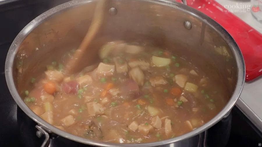 Simmering pot of Guinness chicken stew with vegetables, broth, and fresh herbs visible in a stainless steel pot.