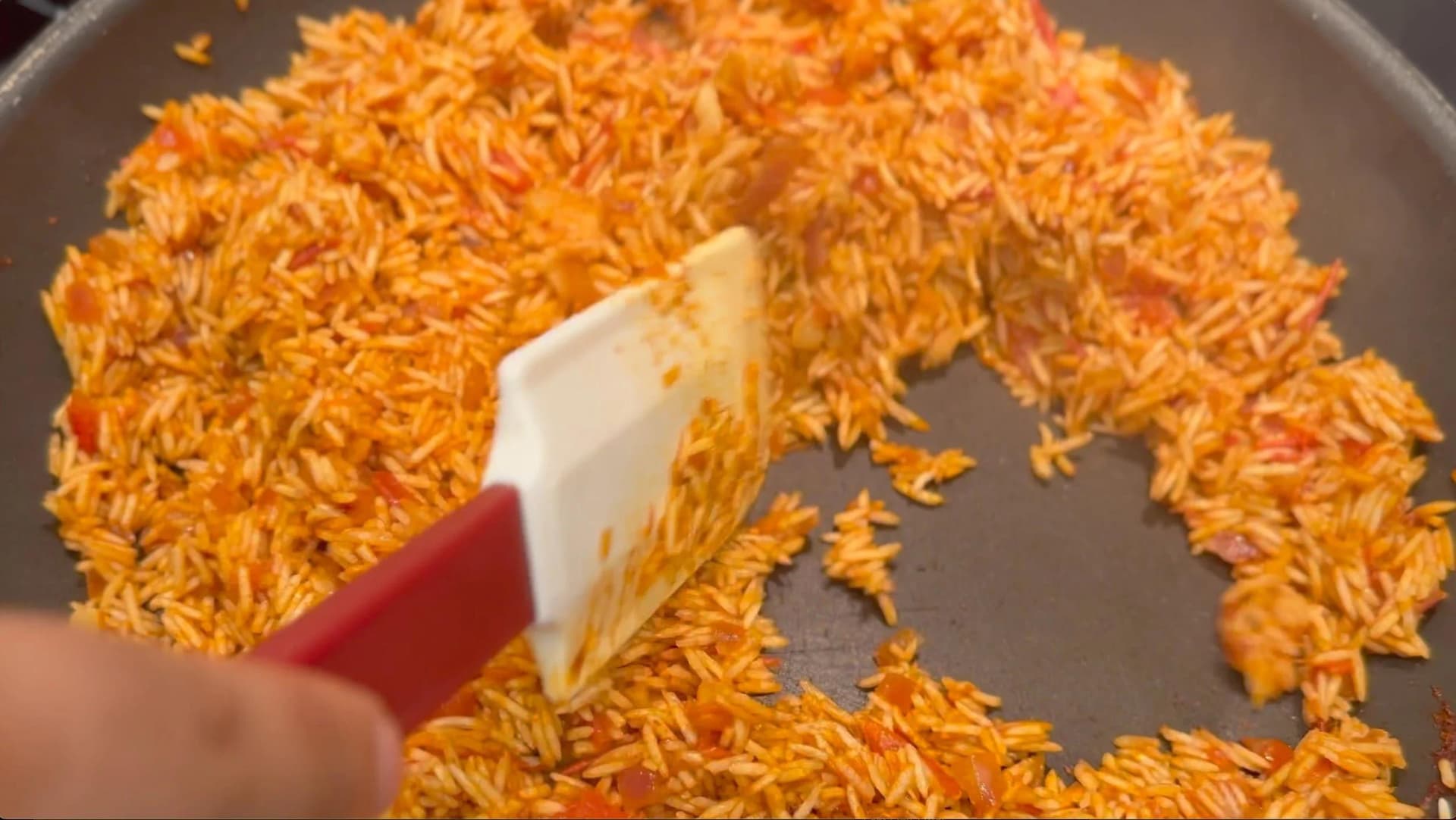 Mixing drained rice into tomato mixture in gray pan with red spatula for Mexican tomato rice.
