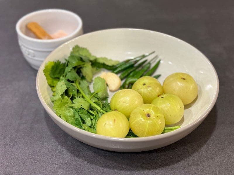 Fresh amla fruits, cilantro, green beans, and ginger arranged in a white bowl for chutney preparation.