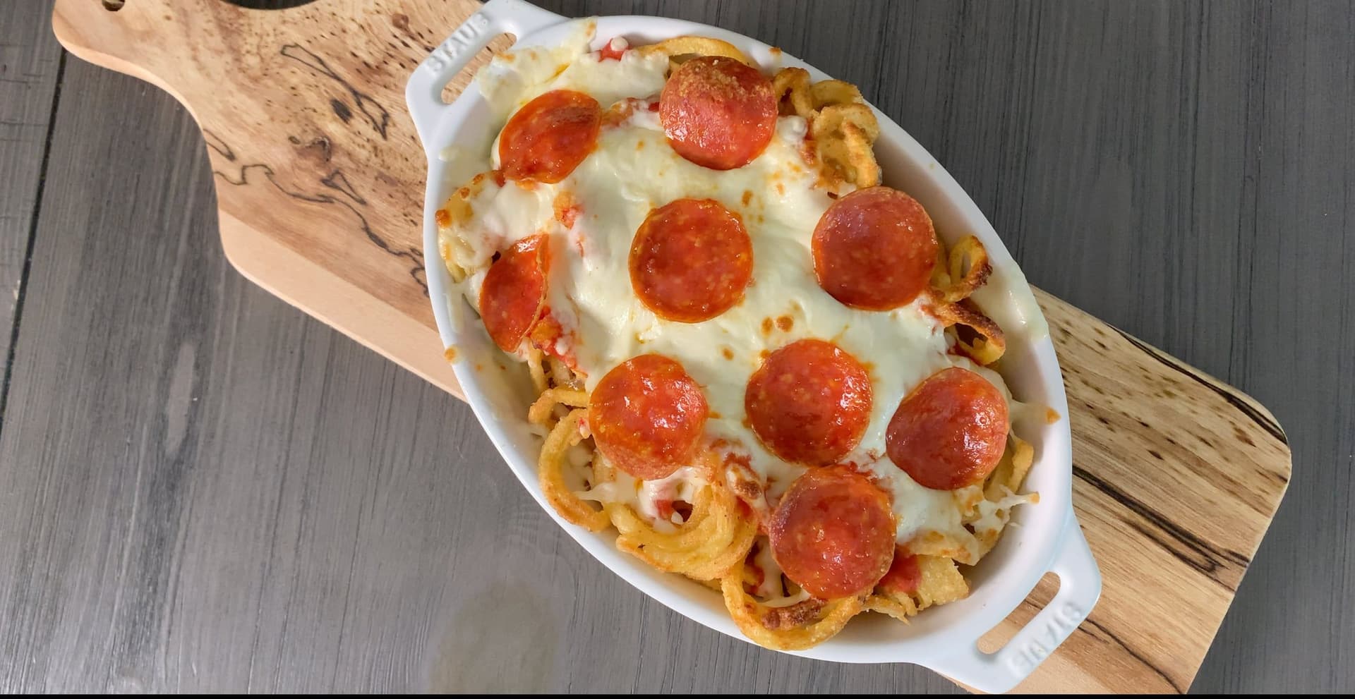 Cheesy pizza fries with curly fries topped with melted cheese and pepperoni slices in a white oval dish.