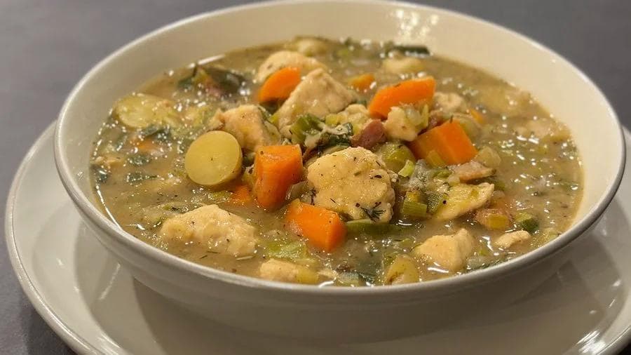 Creamy country harvest chicken stew with tender chicken pieces, diced carrots, potatoes, and herbs in a white bowl.