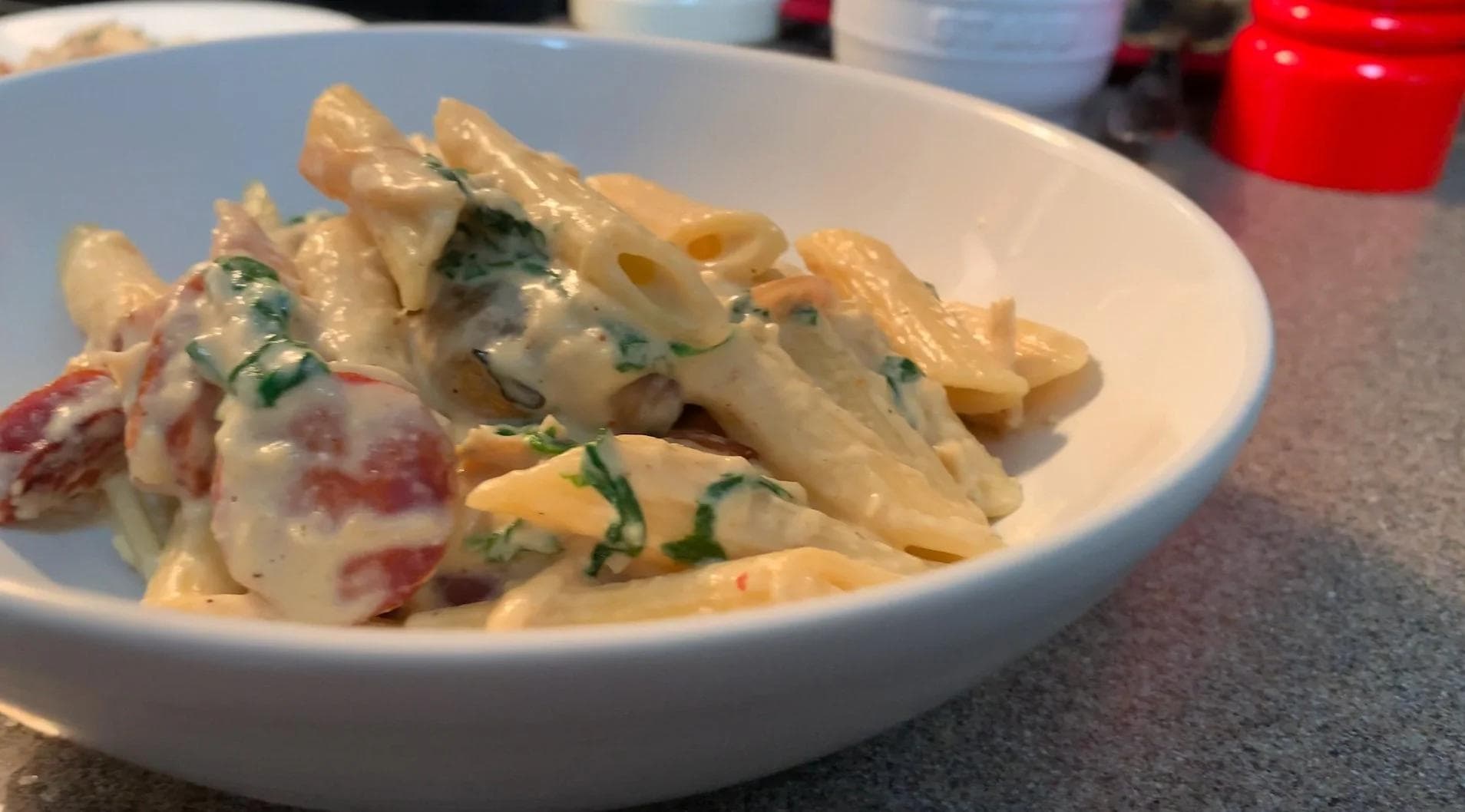 White sauce chicken and chorizo pasta with red pepper pieces and fresh chives in a white bowl.