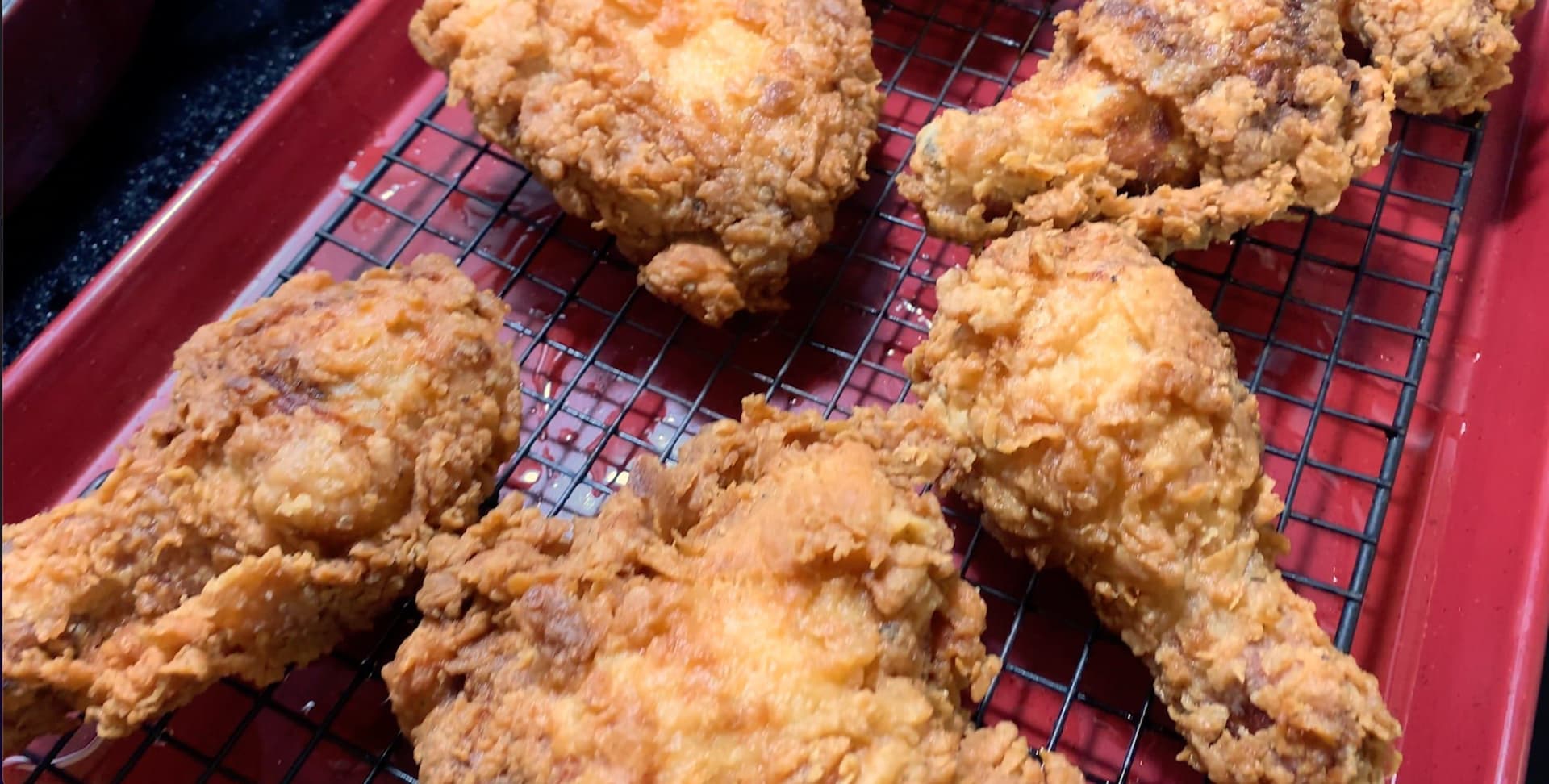 Golden-brown fried chicken pieces cooling on a wire rack lined baking sheet after frying.