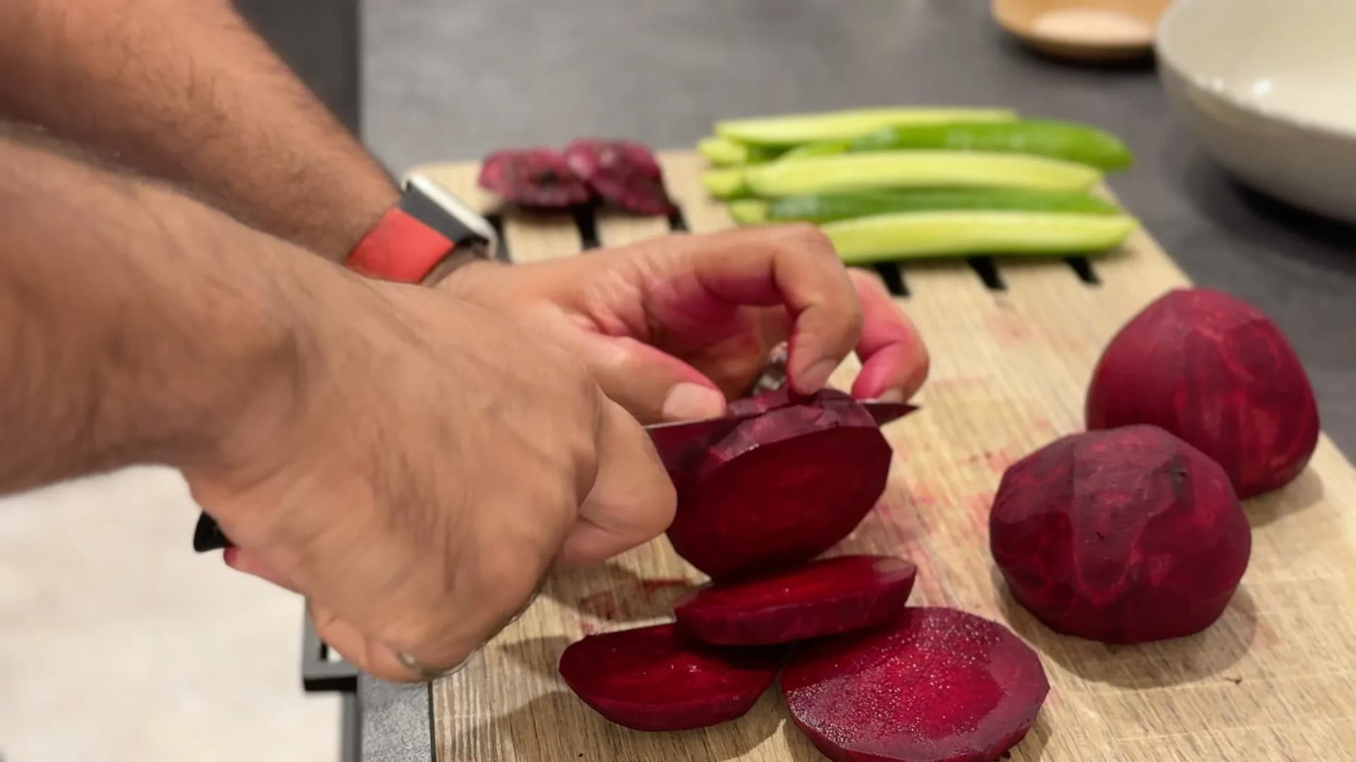 Hands slicing peeled beets into thin strips on a cutting board with green beans and other vegetables nearby.