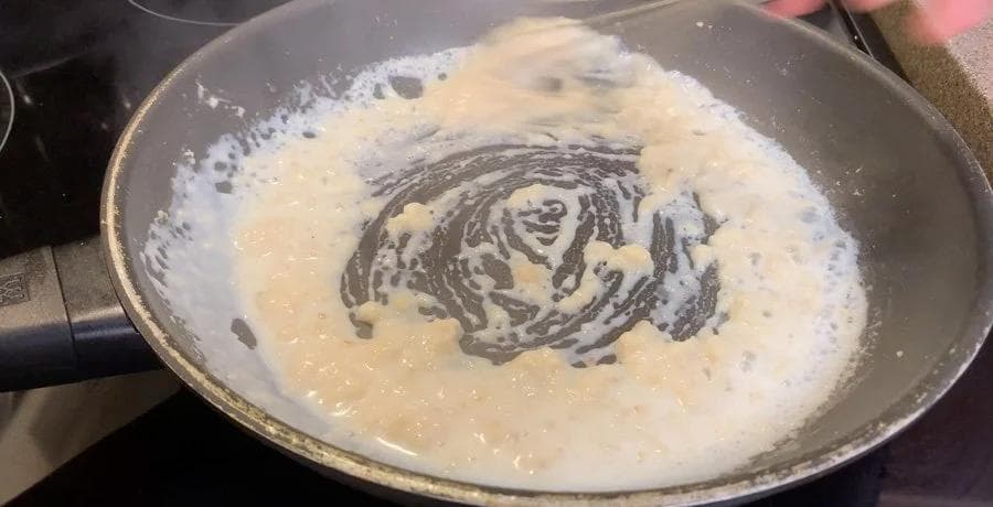 Creamy béchamel sauce simmering in a pan, showing thickened white sauce with swirls of a whisk.