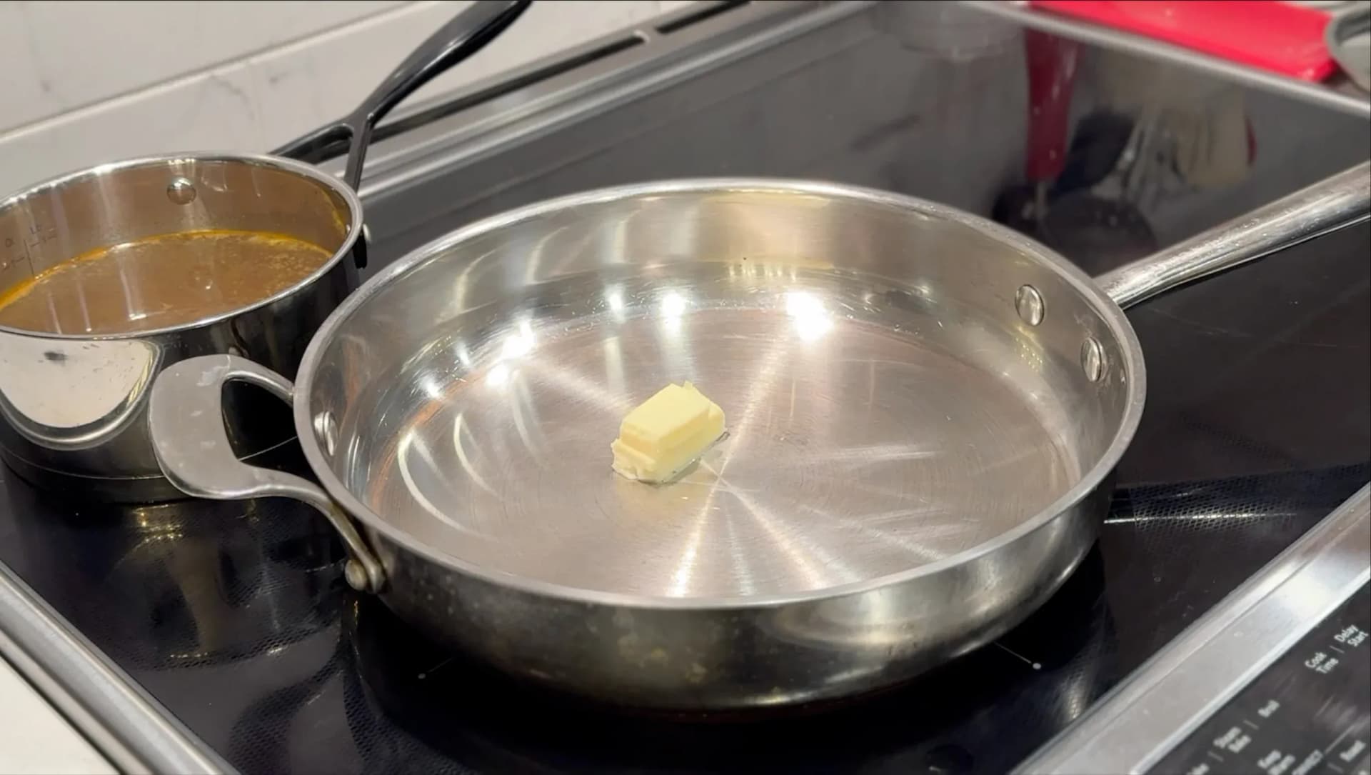 Butter melting in a stainless steel pan on stovetop with measuring cup of broth nearby.